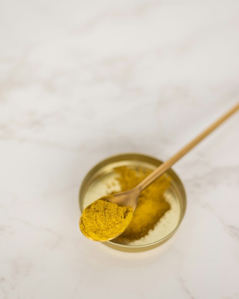 turmeric powder on golden spoon and lid against white neutral countertop for inflammation pain relief and management