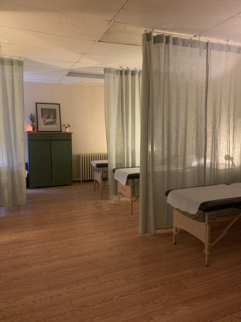 roncys apothecary and clinic community acupuncture room with curtain dividers, treatment tables, and green cabinet with apothecary framed poster in the background toronto